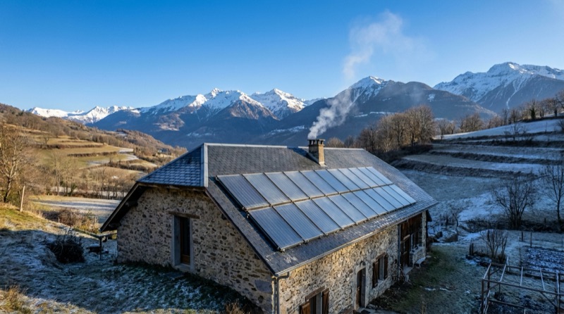 Capteurs solaires thermiques installés sur le toit d'une maison en pierre par temps clair